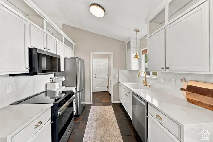Vaulted ceiling kitchen featuring white cabinetry, light countertops, and dark floor tiling