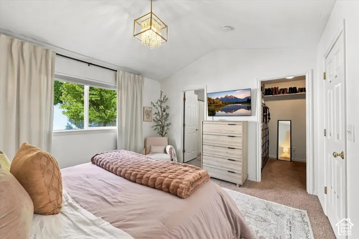 Vaulted ceiling with a contemporary chandelier, window with roller shade, and built-in closet storage