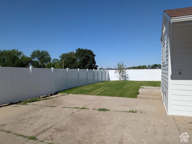Enclosed backyard featuring white fencing, a manicured lawn, and a concrete patio