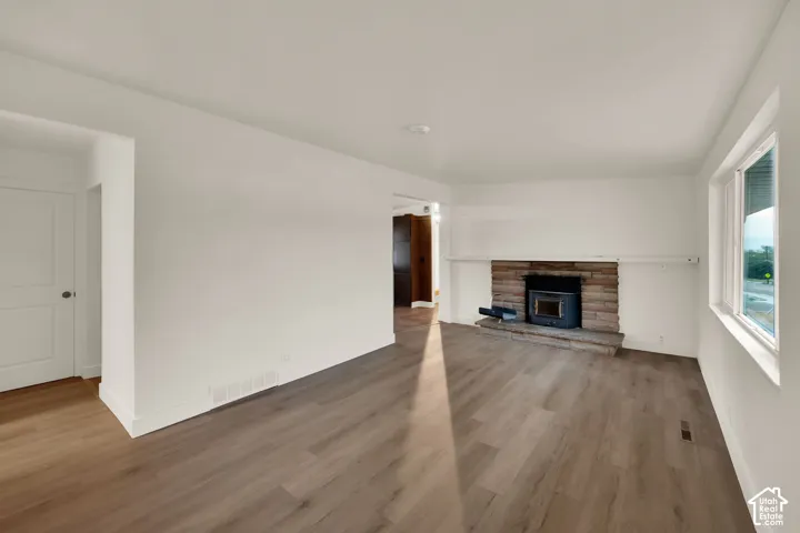 Wood-finish flooring, white painted walls, window with white trim, stone fireplace surround, and dark wood-burning insert