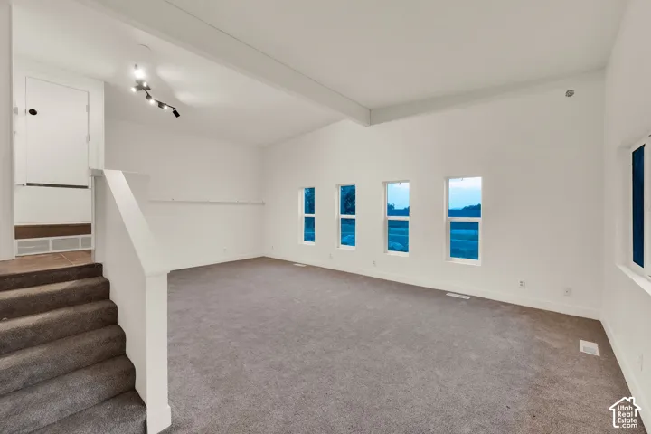 Vaulted ceiling, track lighting, multiple windows, carpet flooring, and staircase with carpeted treads