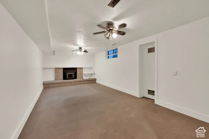 Spacious room featuring a stone-clad fireplace with a hearth, built-in shelving, two ceiling fans, and a white paneled door