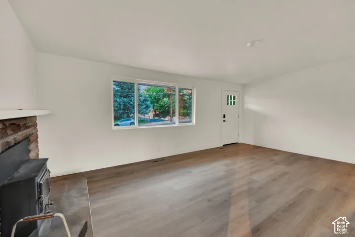 Wood-finish flooring, white walls, and a stone-clad fireplace with a wood-burning stove