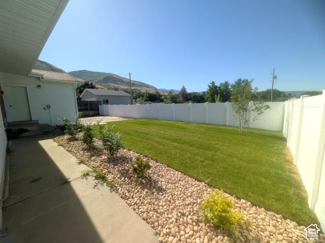 Expansive lawn area, full privacy fencing, established rock landscaping, concrete pathway, and distant mountain backdrop