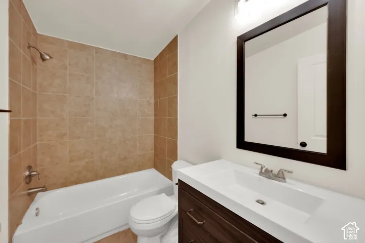 Bathroom featuring a white bathtub, tiled shower surround, dark wood-finish vanity, integrated sink, and framed mirror