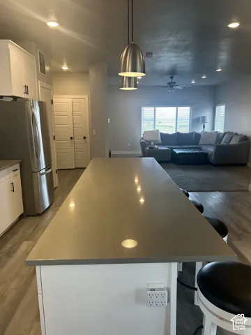 Expansive kitchen island with a neutral-toned countertop, white cabinetry with dark hardware, stainless steel refrigerator, and wood-finish flooring
