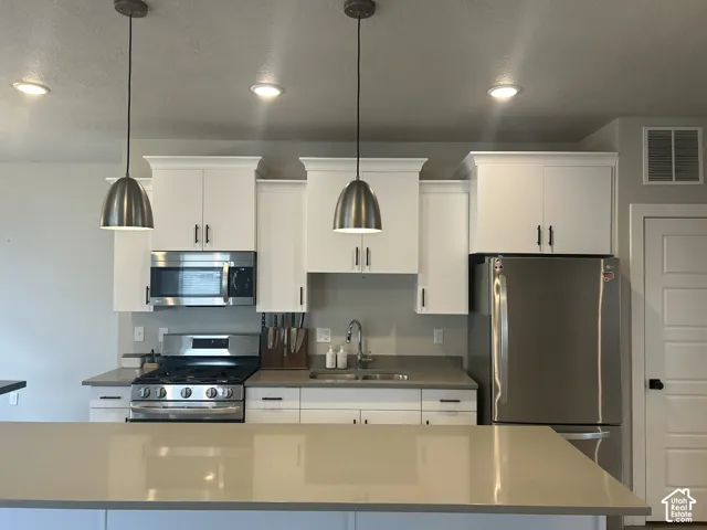 Contemporary kitchen featuring white cabinetry, stainless steel appliances, pendant lighting, recessed lighting, and light-toned countertops