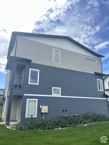 Multi-level exterior featuring grey stucco, blue siding, a balcony with dark railings, and ground-level landscaping