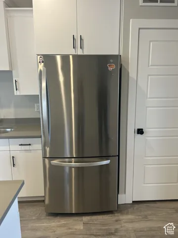 Stainless steel refrigerator with bottom freezer, white flat-panel cabinetry, wood-finish flooring, and white interior door with black hardware
