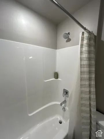 Bathtub with an integrated shower, chrome fixtures, and white wall surround