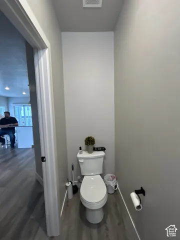 White toilet with a wall-mounted toilet paper holder and wood-finish flooring