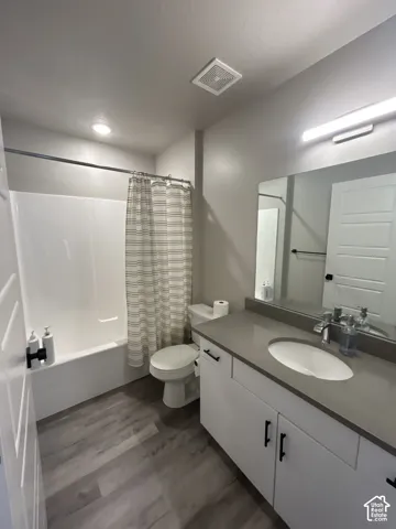 Bathroom featuring a single vanity with stone countertop, white cabinetry, integrated sink, and wood-finish flooring