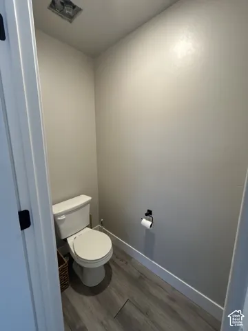 White toilet with a white seat, wood-finish flooring, and a matte black toilet paper holder