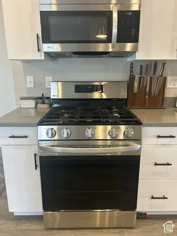 Stainless steel oven with gas cooktop, stainless steel microwave, white cabinetry with black hardware, and light-toned countertops
