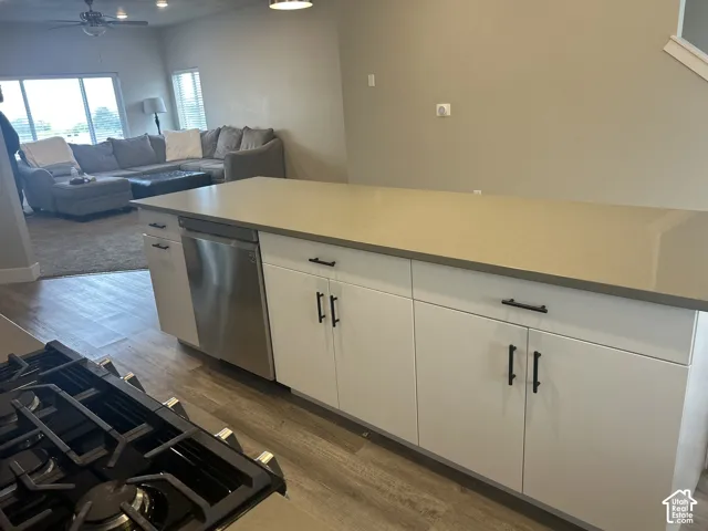 Kitchen island with integrated stainless steel dishwasher, white cabinetry, dark hardware, and a smooth countertop