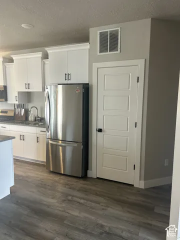White cabinetry with crown molding, stainless steel refrigerator, dark wood-finish flooring, and a paneled interior door