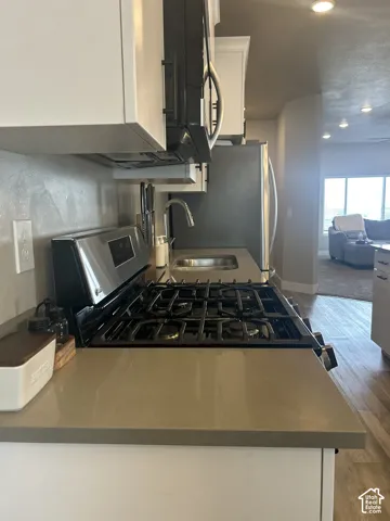 Kitchen featuring white upper cabinetry, stainless steel appliances, a gas range, and a single-basin sink with a gooseneck faucet