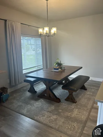 Dining area featuring a contemporary chandelier, large window with blinds, and wood-finish flooring