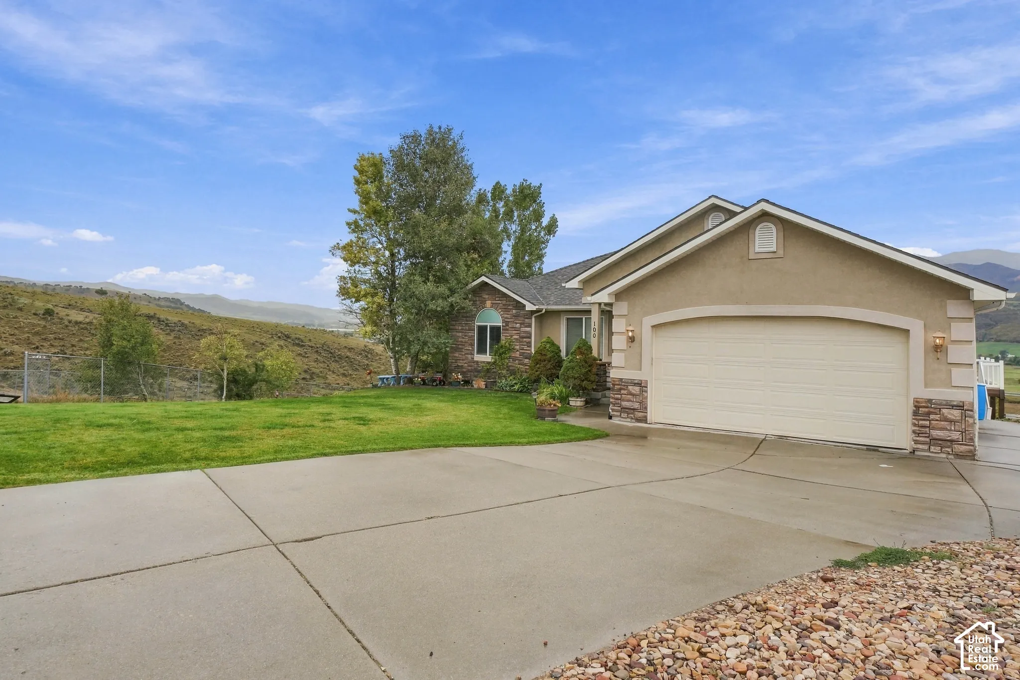 Stucco and stone facade with an arched garage door, concrete driveway, and established landscaping