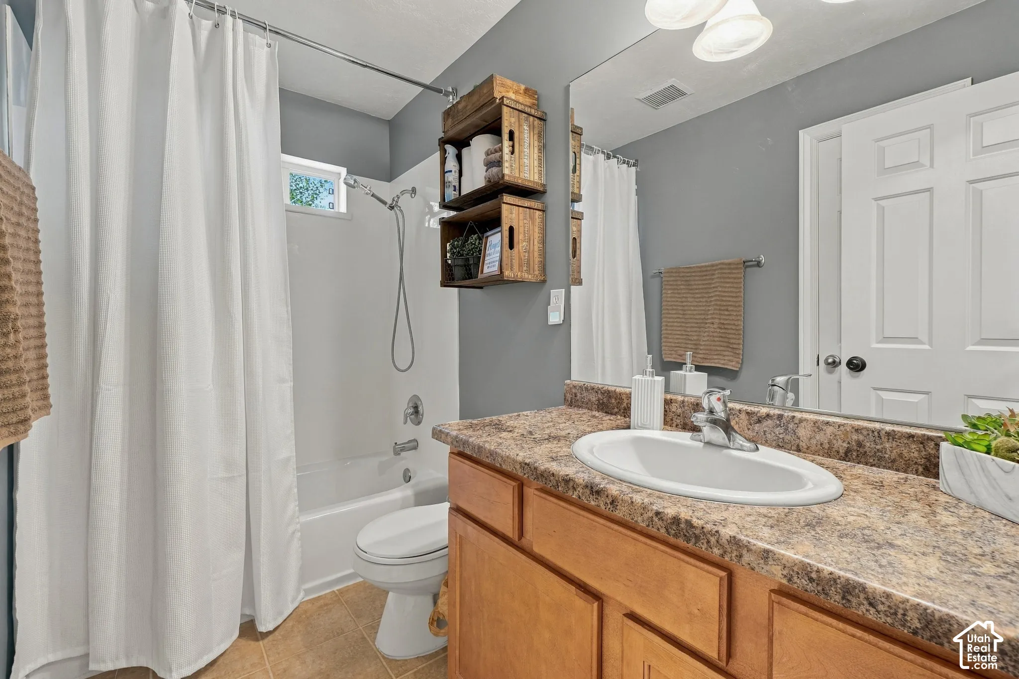 Bathroom featuring a wood-finish vanity with a built-in sink and speckled countertop, a full mirror, and a shower-over-tub combination with a window