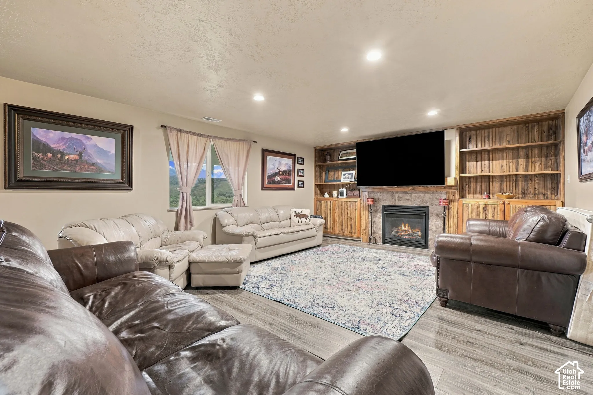 Spacious living area featuring wood-finish flooring, a stone-surround fireplace, and built-in shelving