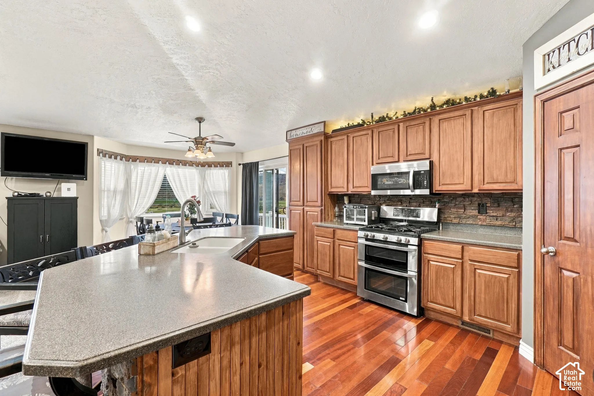 Kitchen featuring hardwood flooring, stainless steel appliances, wood cabinetry, and a stone-finish backsplash