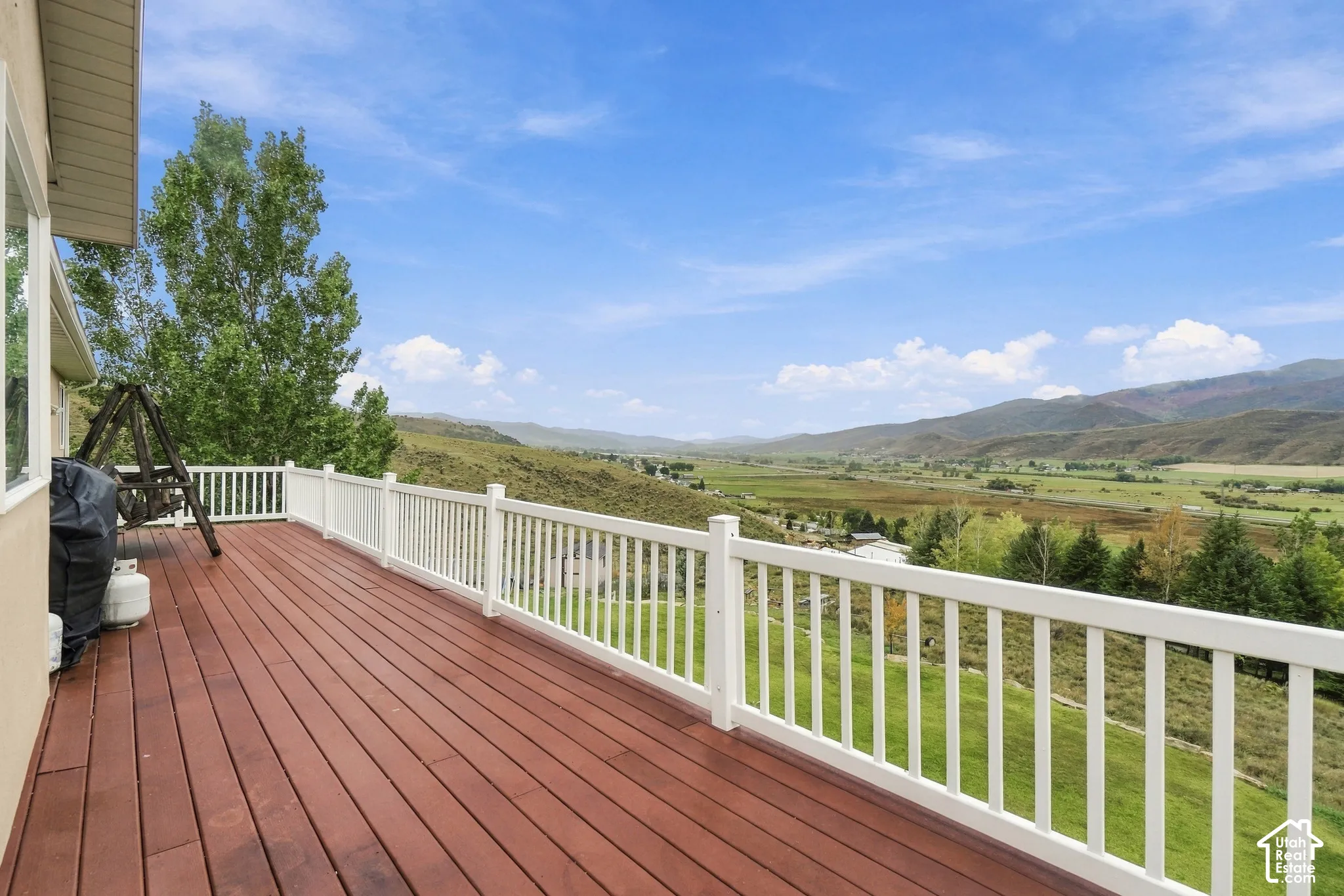 Expansive wood-finish deck with white railings, offering clear mountain and valley scenery