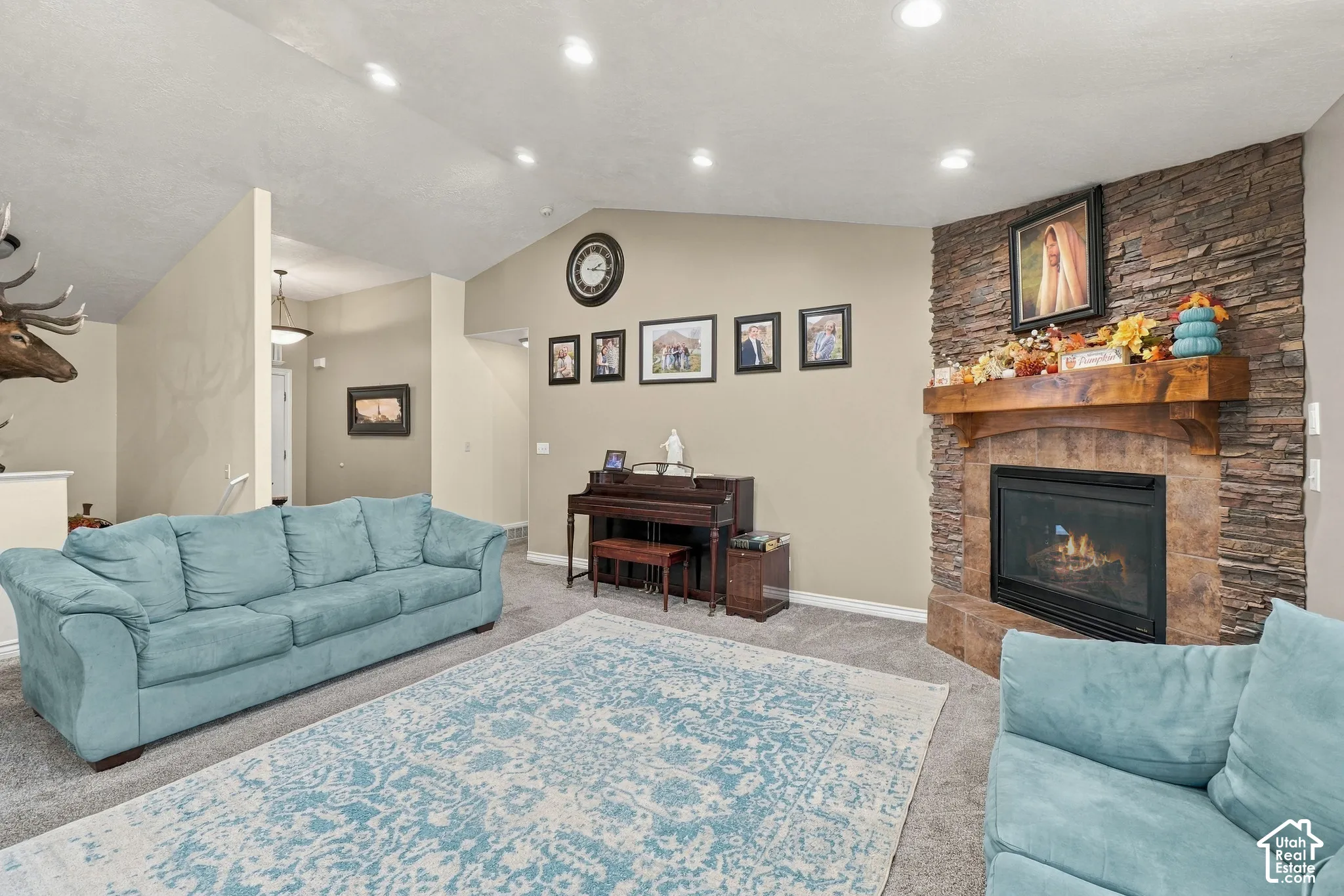 Vaulted ceiling, recessed lighting, carpet flooring, stone-clad fireplace with wood mantel, and built-in shelving