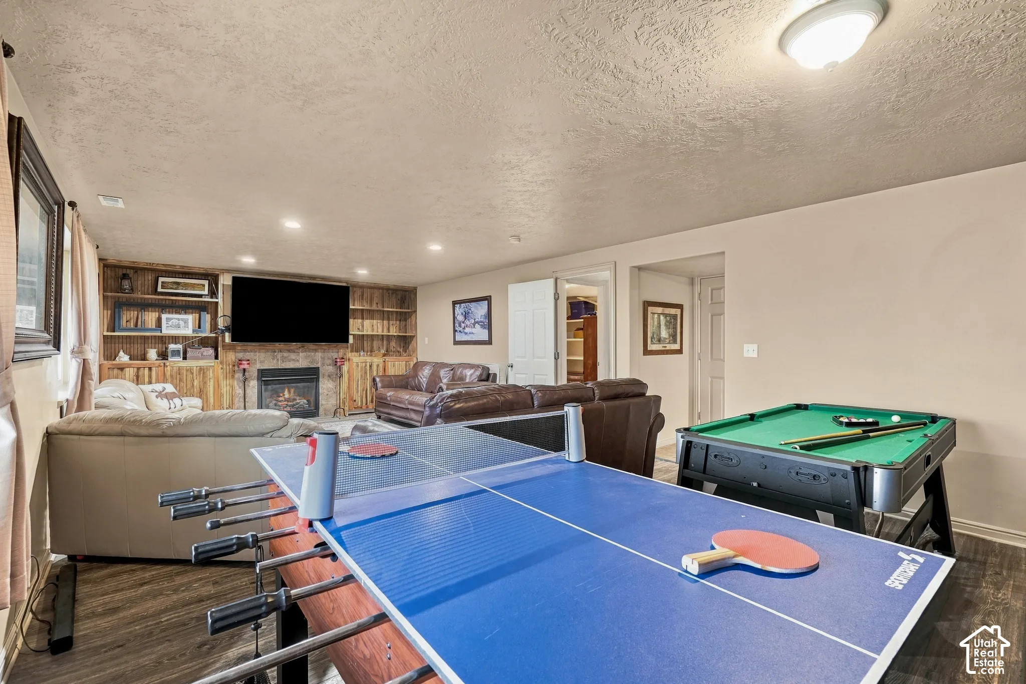 Spacious recreation area featuring a built-in entertainment center, fireplace with stone surround, recessed lighting, and wood-finish flooring