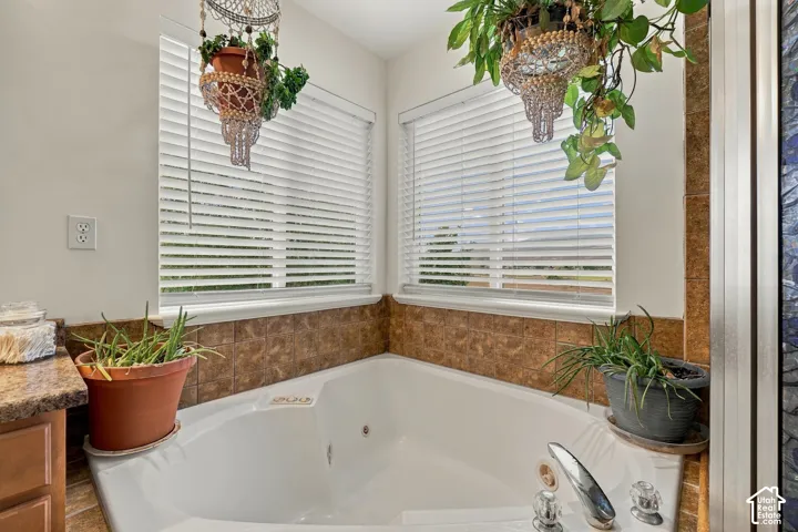 Large jetted tub with tile surround, dual windows, and built-in cabinetry