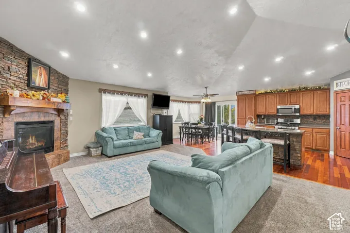 Expansive open-concept living space with a stone-clad fireplace and wood mantle, recessed ceiling lights, and a kitchen featuring wood cabinetry and stainless-steel appliances