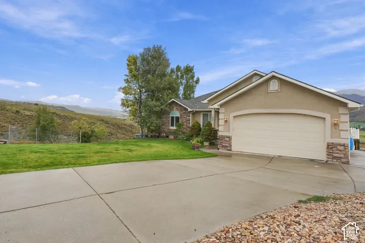 Stucco and stone facade with an arched garage door, concrete driveway, and established landscaping