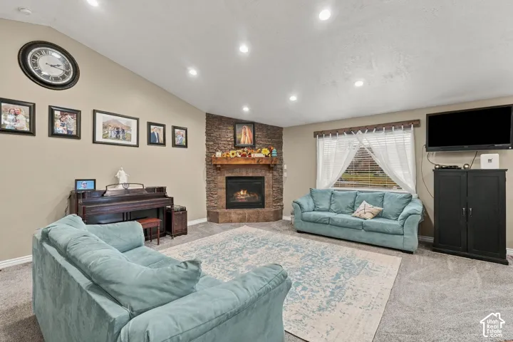 Vaulted ceiling with recessed lighting, stone-clad fireplace with mantel, window with blinds, and carpeted flooring