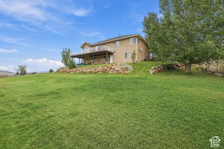 Expansive green lawn with a two-story residence featuring a full-width upper deck and lower-level patio