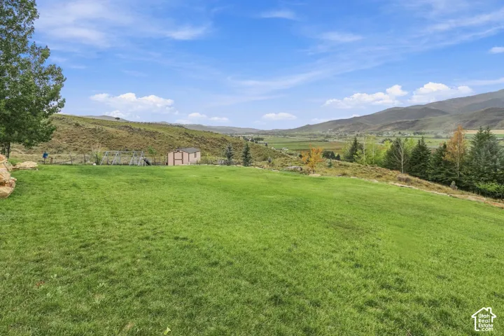 Expansive grassy area with a storage shed, mature trees, and a distant mountain landscape
