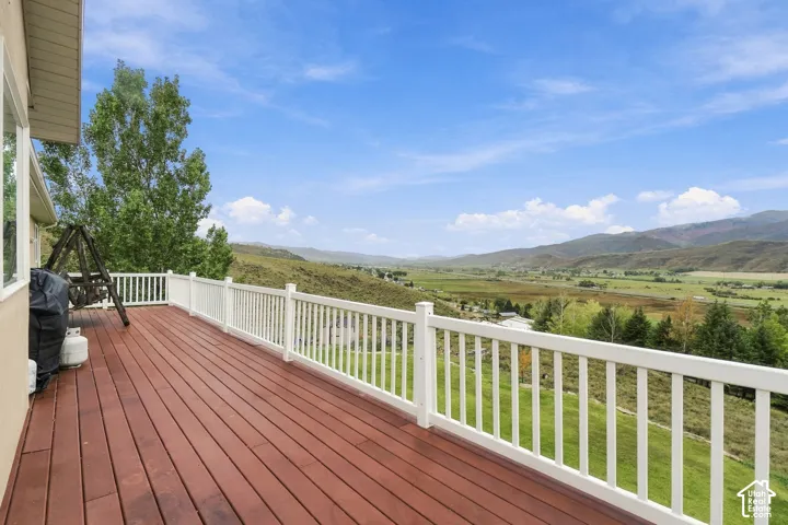 Expansive wood-finish deck with white railings, offering clear mountain and valley scenery