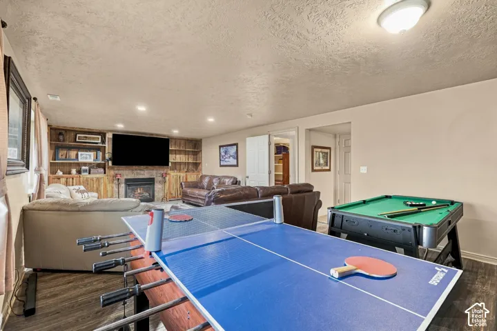 Spacious recreation area featuring a built-in entertainment center, fireplace with stone surround, recessed lighting, and wood-finish flooring