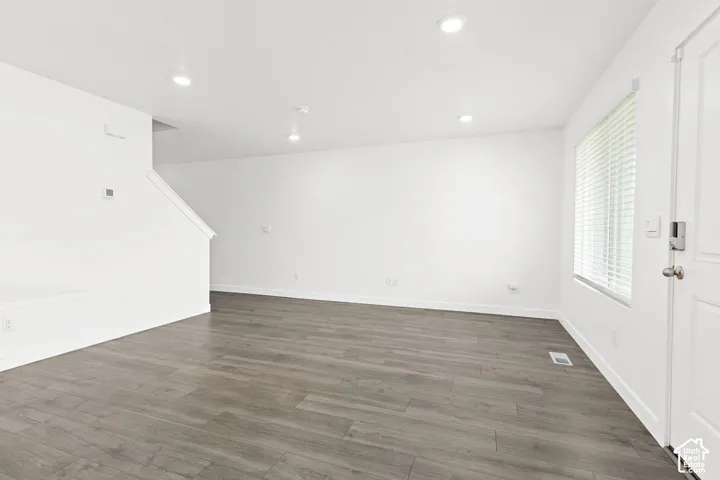 Spacious room featuring wood-finish flooring, white walls, recessed ceiling lighting, and a white paneled door