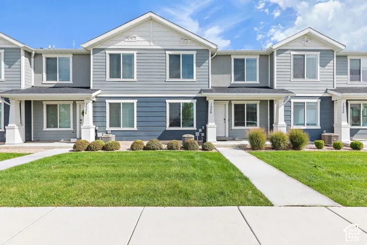 Modern townhome exterior featuring gray siding, white trim, a covered porch, and a concrete pathway