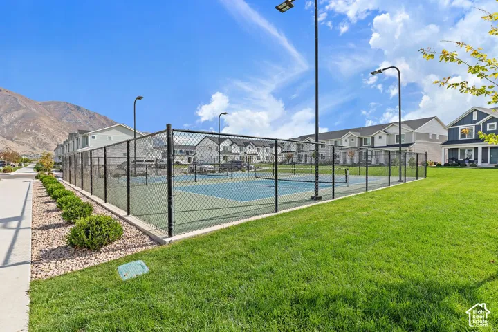 Community tennis court featuring a chain-link fence, hard court surface, and overhead lighting