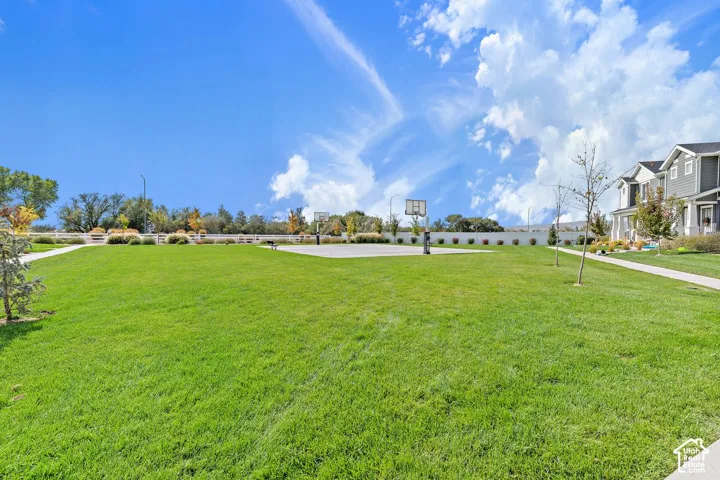 Expansive green space featuring a paved court with basketball hoops, a concrete walking path, and mature landscaping