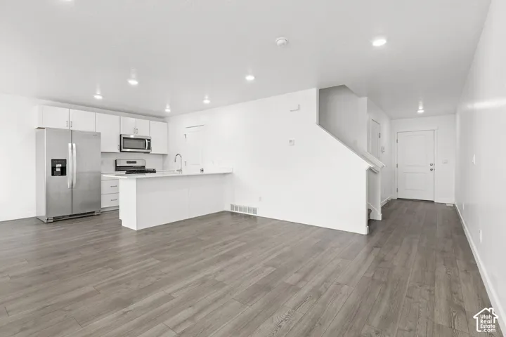 Open-concept kitchen and living area featuring wood-finish flooring, white cabinetry, a stainless steel appliance suite, and a staircase with a white railing