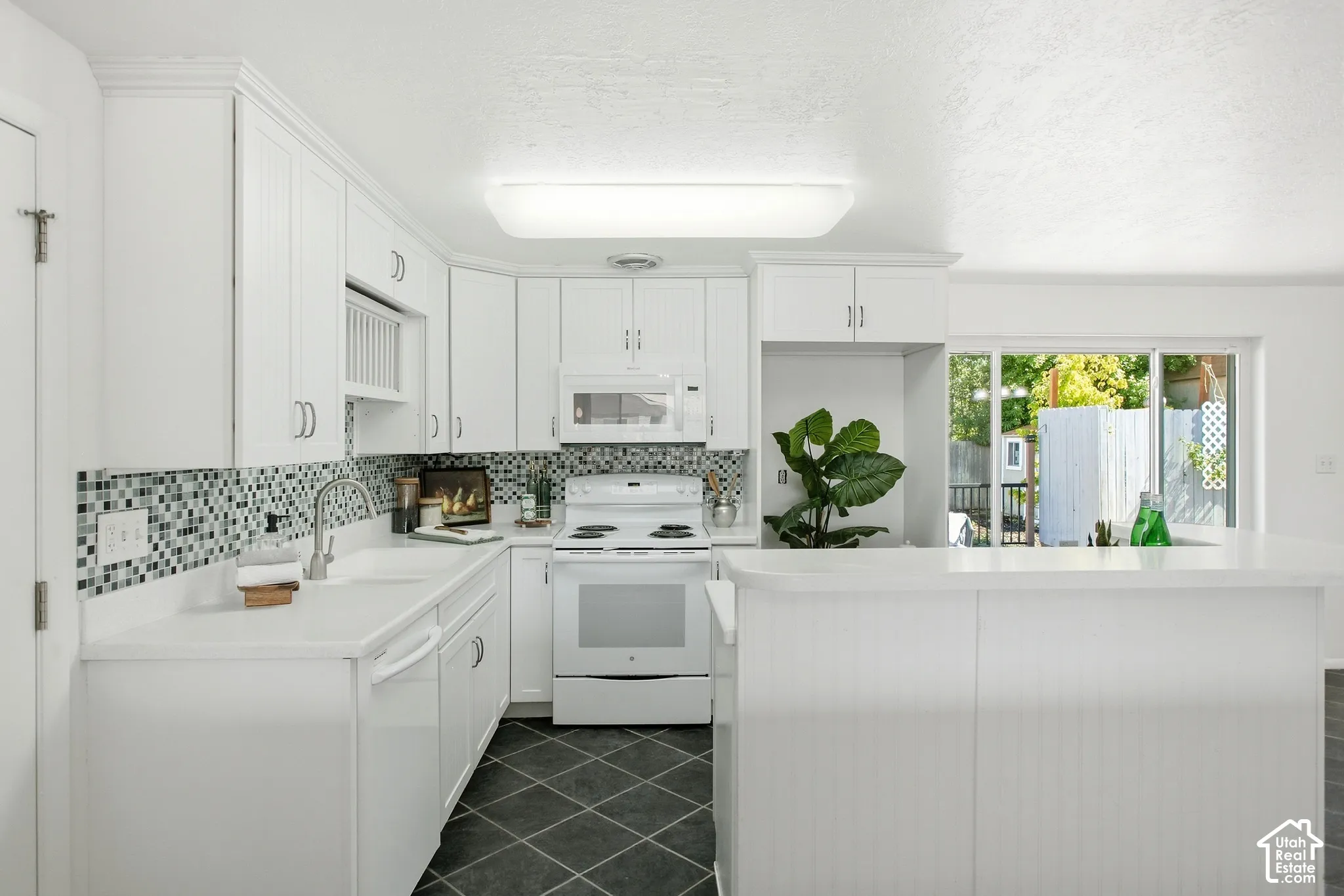White kitchen cabinetry with brushed nickel hardware, mosaic tile backsplash, white countertops, and a built-in kitchen island