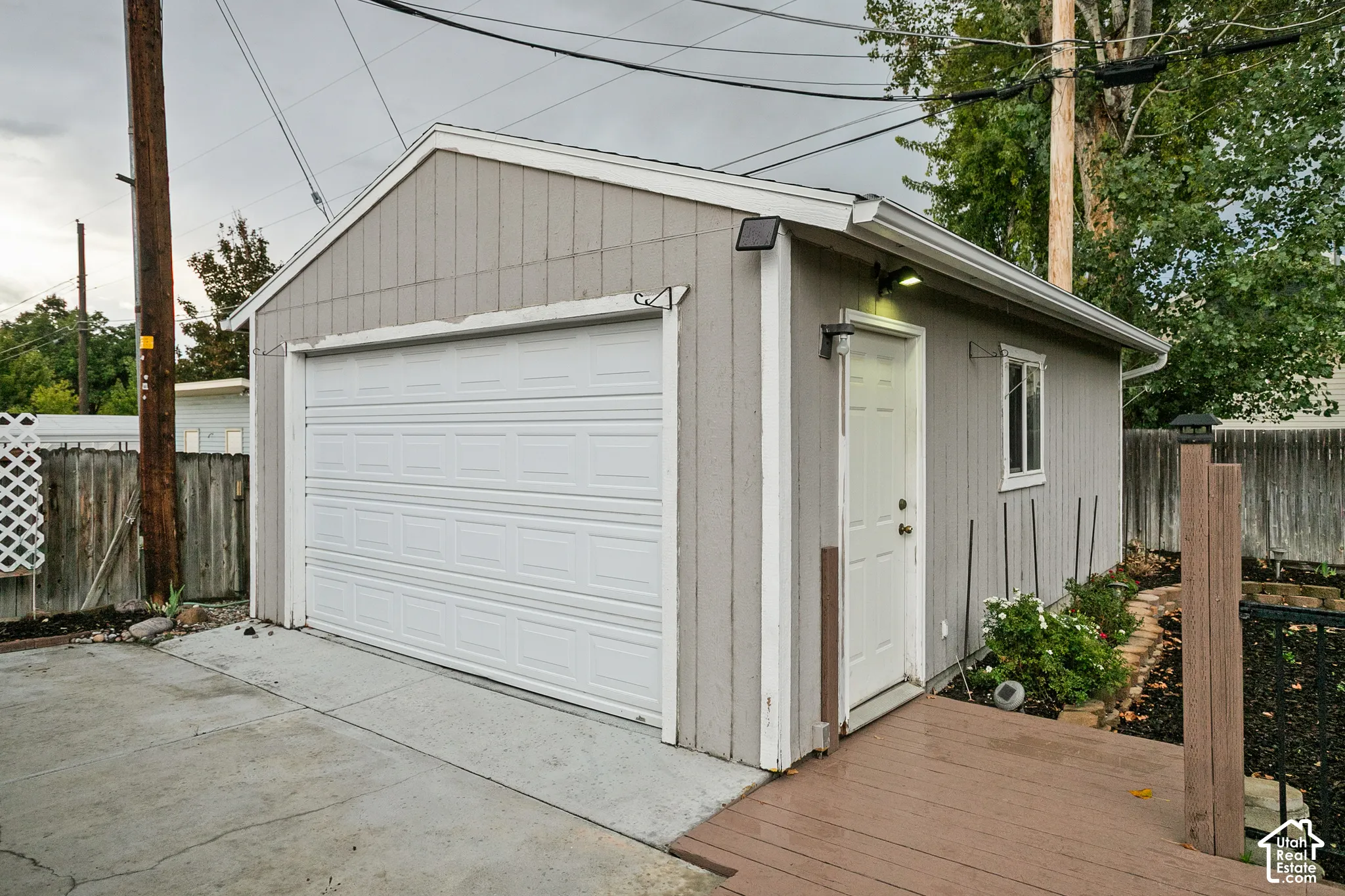 Detached garage with a paneled overhead door, a side entry door, and a wood-finish deck