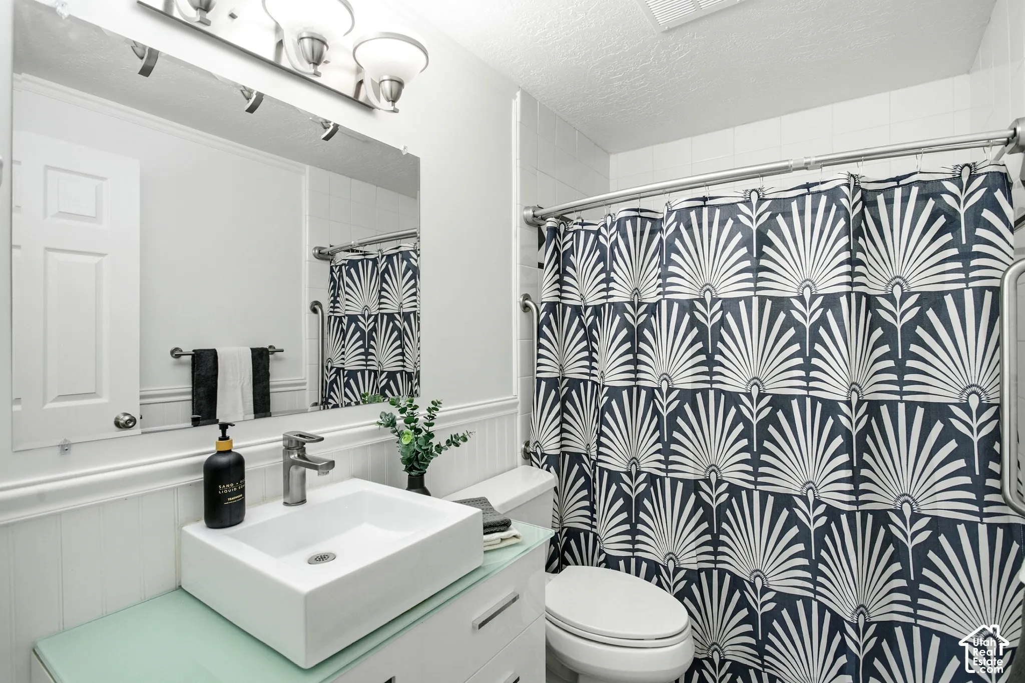 Bathroom featuring a vessel sink, single-handle faucet, wainscoting, and a shower with a grab bar