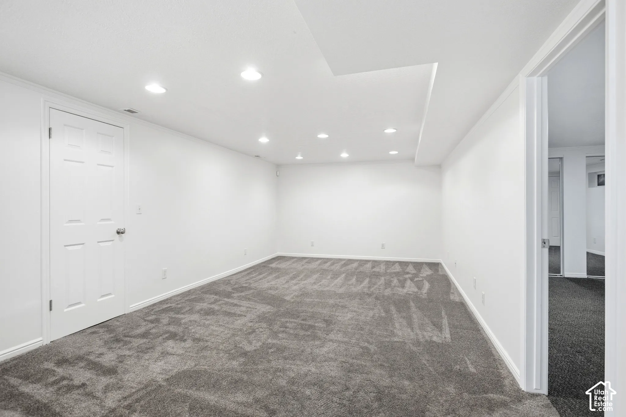Spacious room featuring neutral carpeting, recessed ceiling lighting, and crisp white walls