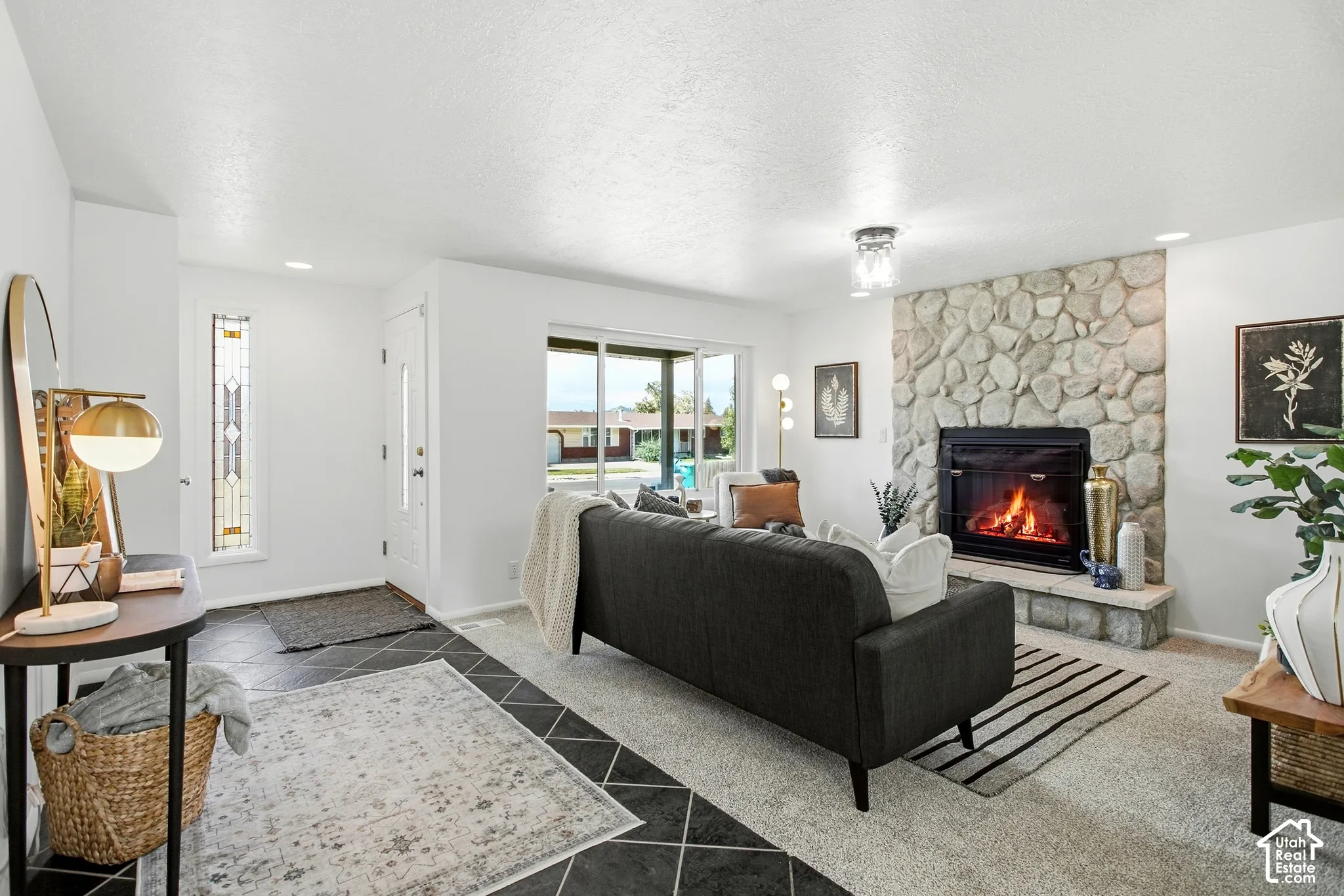 Stone-clad fireplace with hearth, large glass sliding door, decorative front door with side light, recessed lighting, and mixed flooring