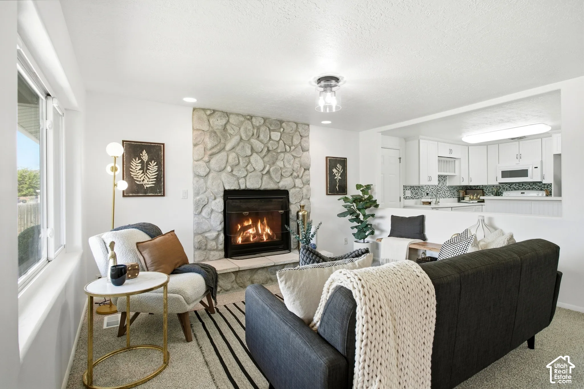 Stone-clad fireplace with hearth, white window frames, recessed lighting, and kitchen pass-through with white cabinetry