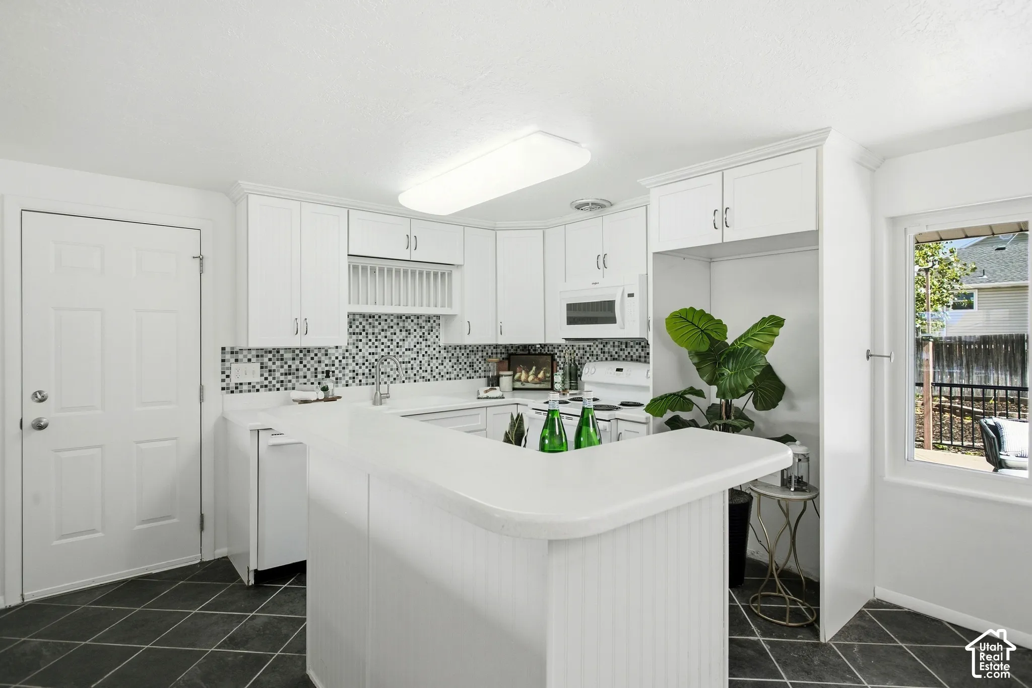 White cabinetry with beadboard paneling, mosaic tile backsplash, solid surface countertops, and dark square tile flooring