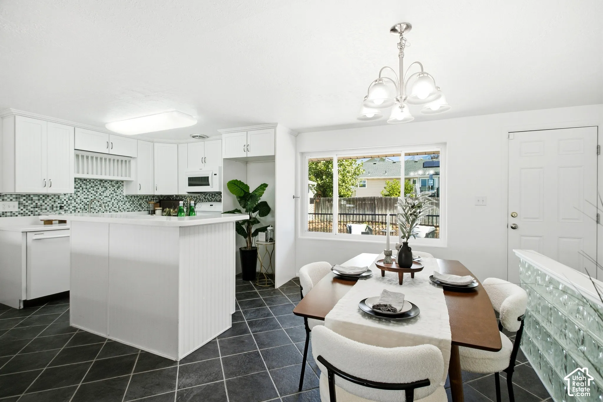 Kitchen and dining area featuring white cabinetry, a kitchen island with a white countertop, a mosaic tile backsplash, and dark diamond-patterned floor tiles